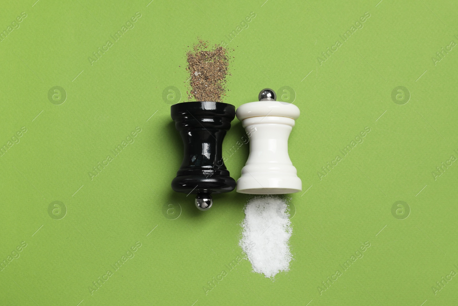 Photo of Salt and pepper shakers on green table, flat lay