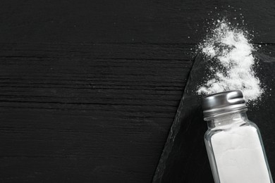 Photo of Salt shaker on black wooden table, top view. Space for text