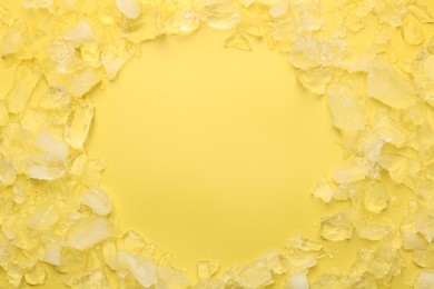 Frame of crushed ice on yellow background, flat lay. Space for text