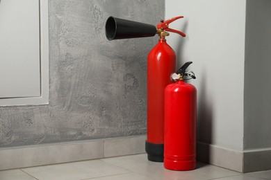 Photo of Fire extinguishers on floor near grey wall indoors