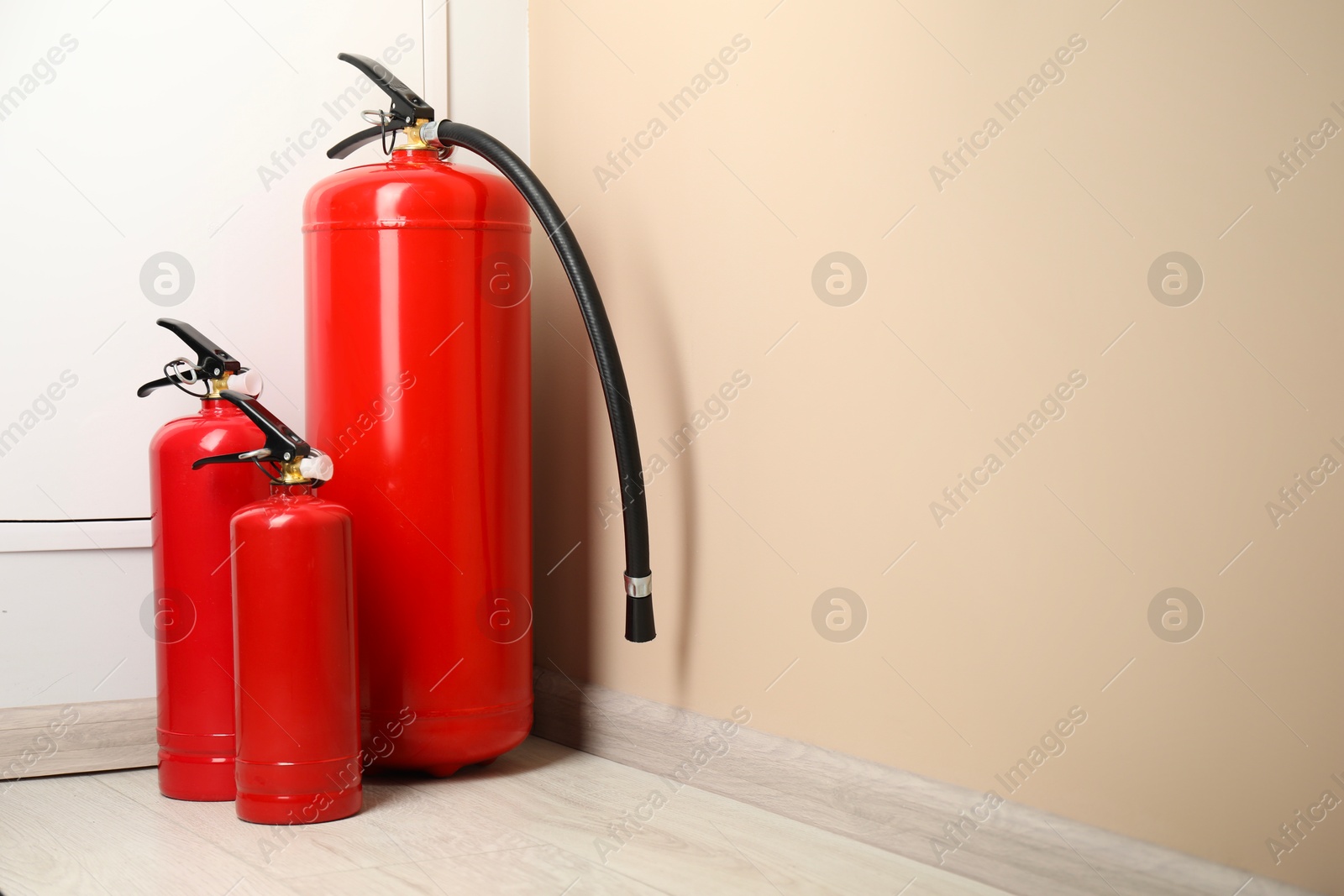 Photo of Fire extinguishers on floor near beige wall indoors