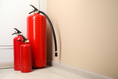 Fire extinguishers on floor near beige wall indoors