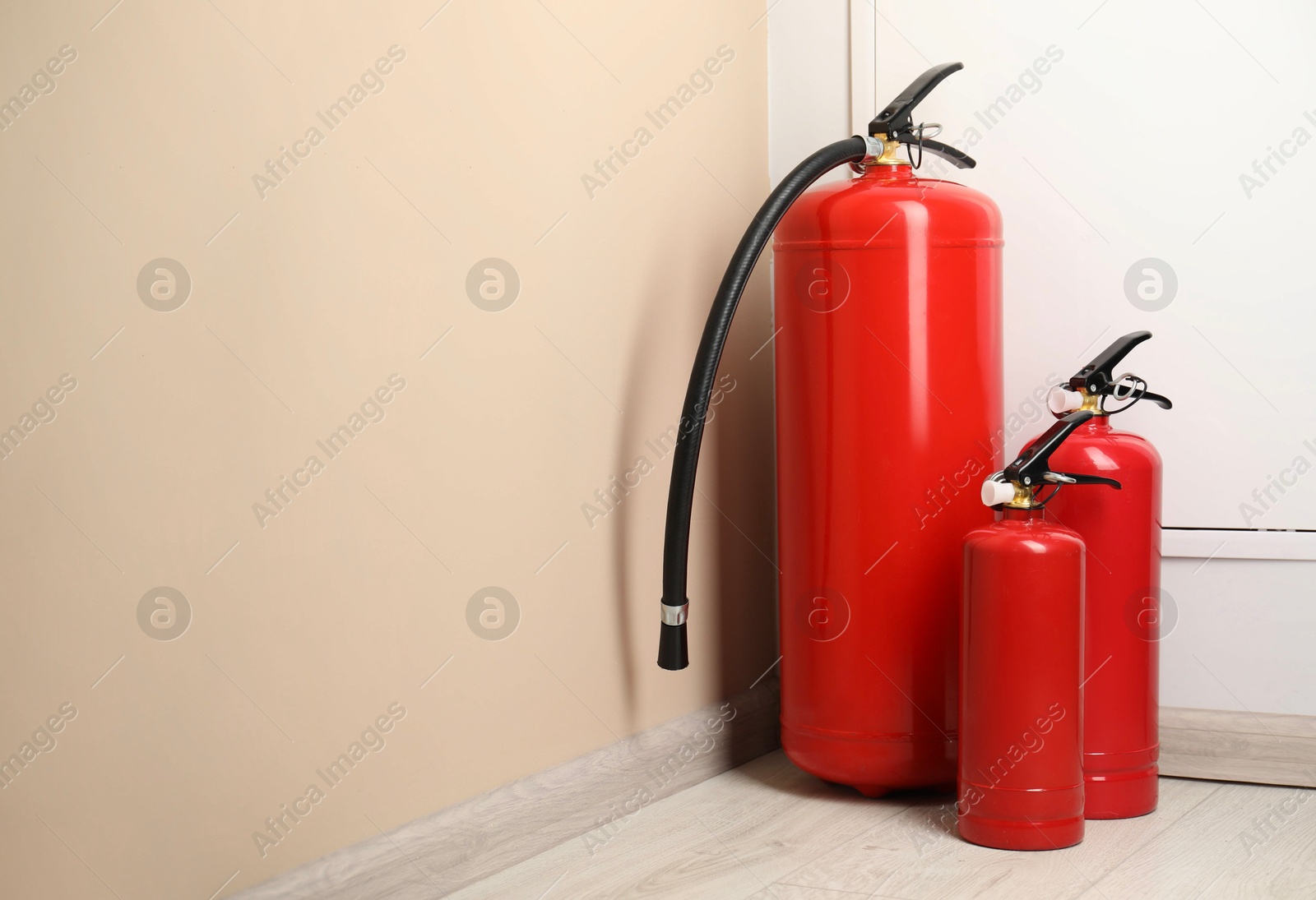 Photo of Fire extinguishers on floor near beige wall indoors