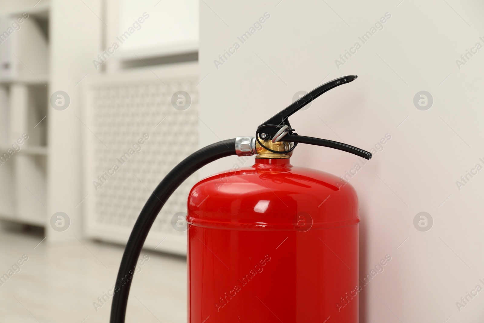 Photo of Fire extinguisher near light wall indoors, closeup