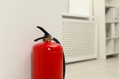 Photo of Fire extinguisher near light wall indoors, space for text