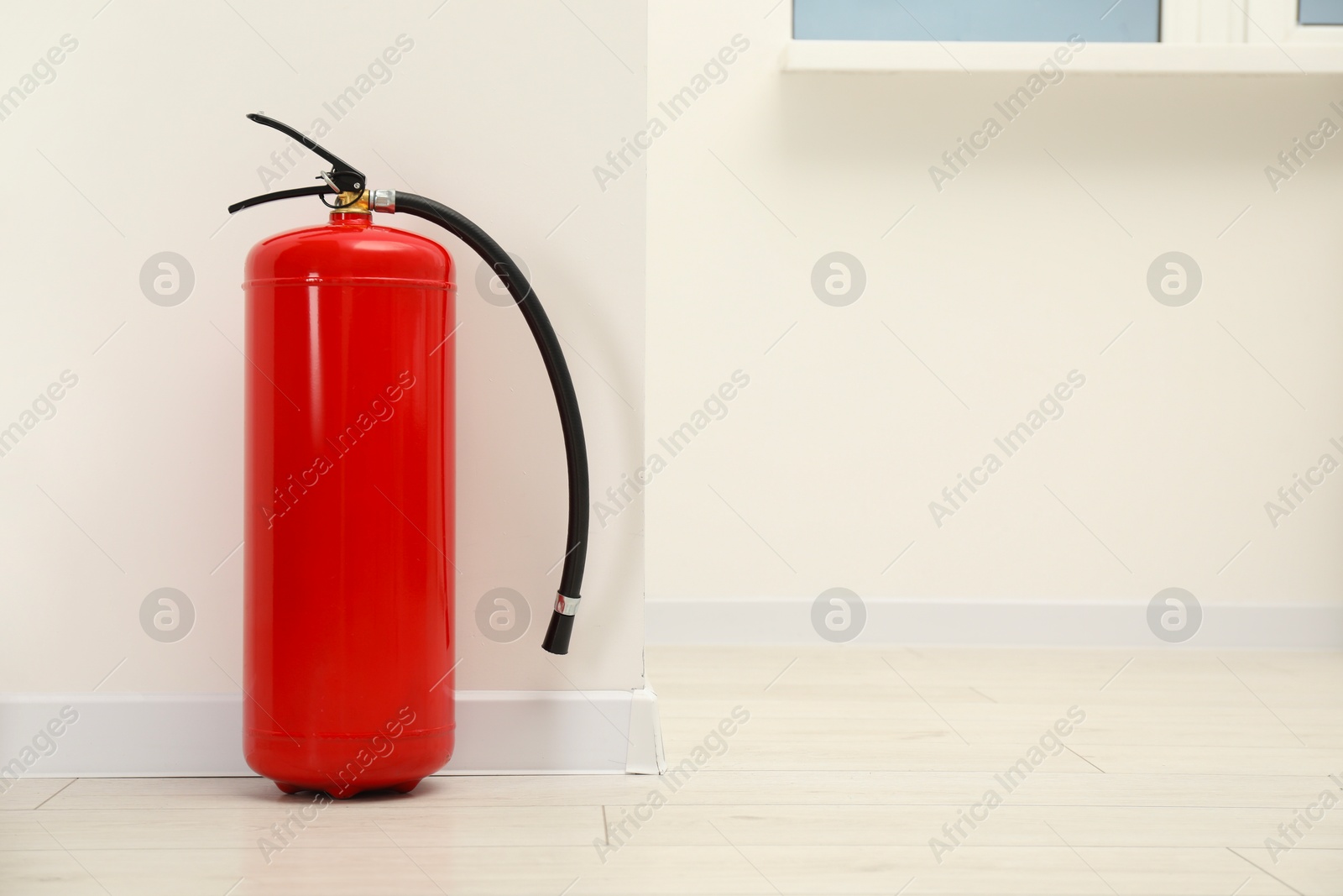 Photo of Fire extinguisher on floor near light wall indoors, space for text