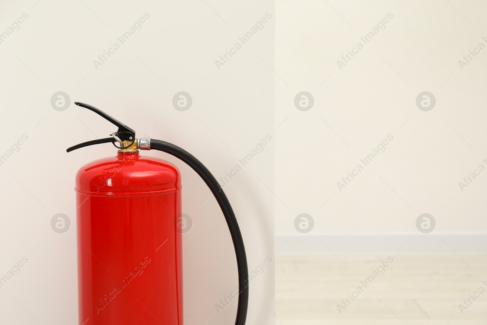 Photo of Fire extinguisher near light wall indoors, space for text