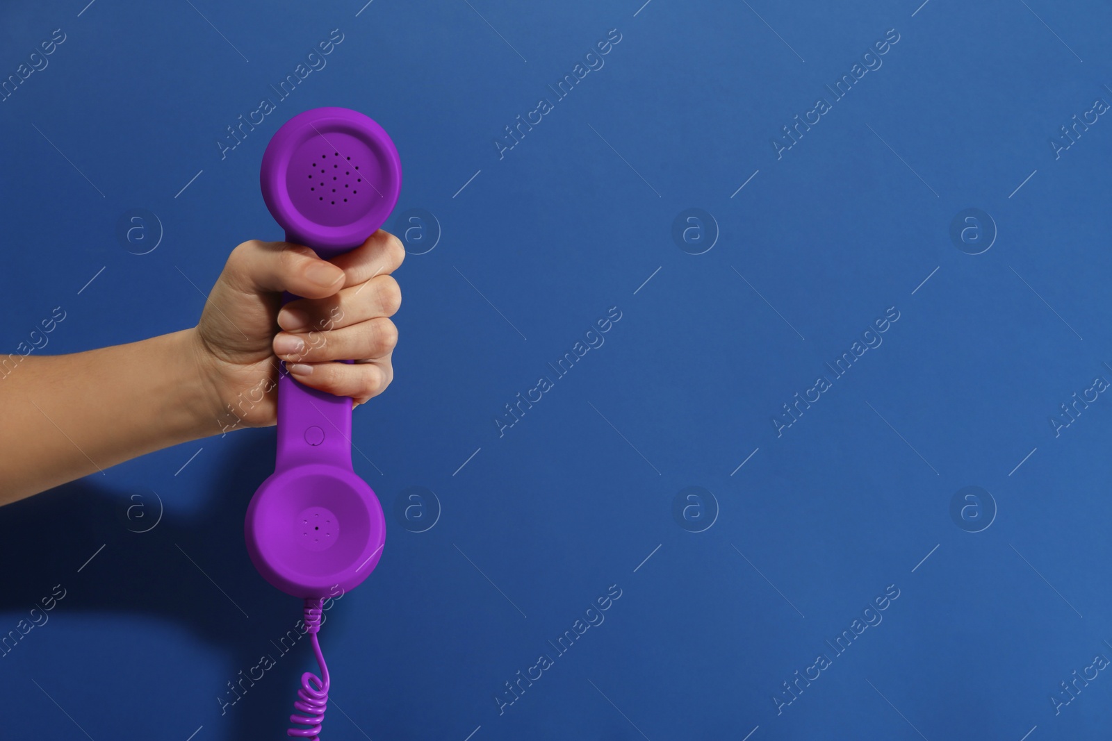 Image of Woman holding purple telephone handset on blue background, closeup. Space for text