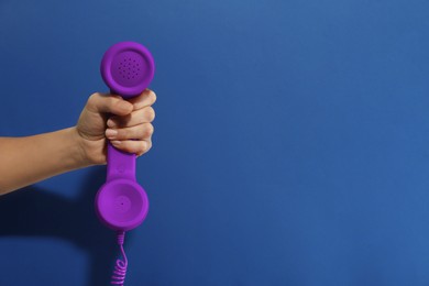 Image of Woman holding purple telephone handset on blue background, closeup. Space for text