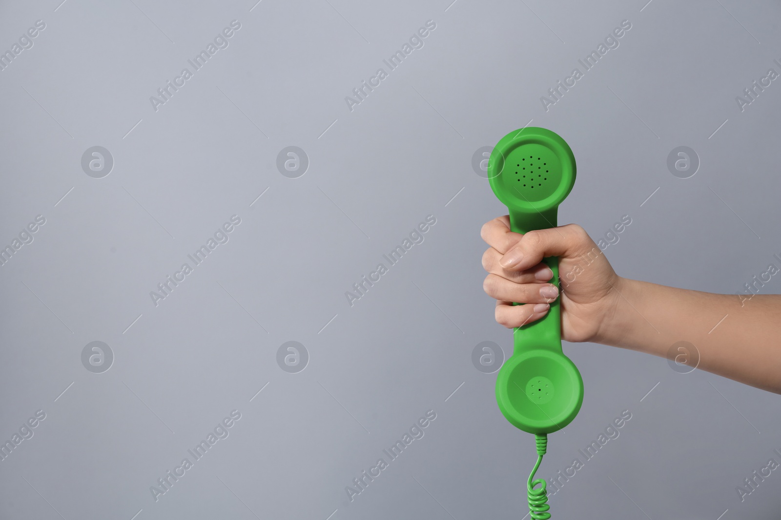 Image of Woman holding green telephone handset on light grey background, closeup. Space for text