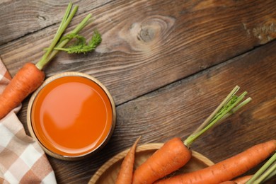 Photo of Healthy carrot juice in glass and fresh vegetables on wooden table, top view. Space for text