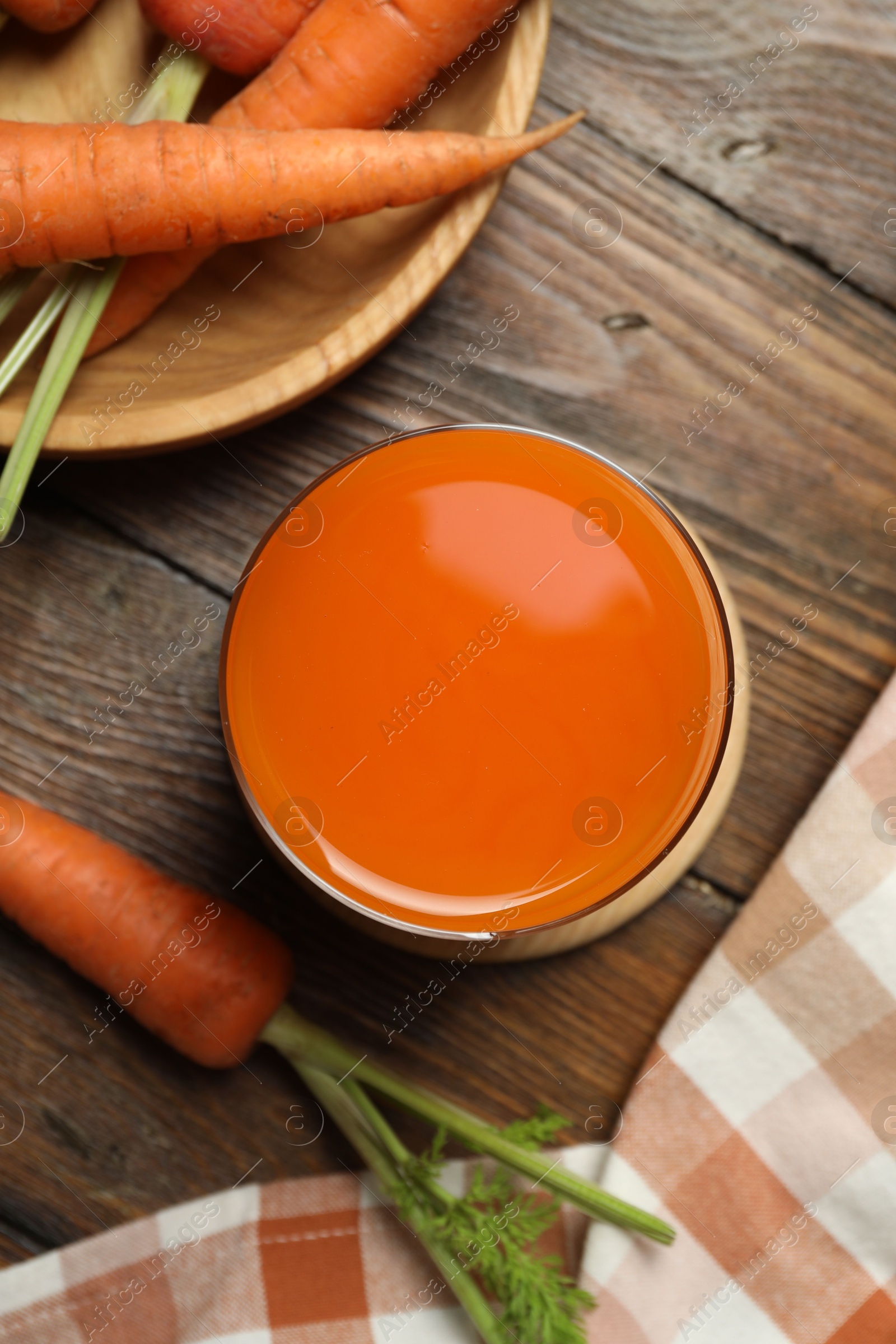 Photo of Healthy carrot juice in glass and fresh vegetables on wooden table, top view