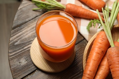 Photo of Healthy carrot juice in glass and fresh vegetables on wooden table