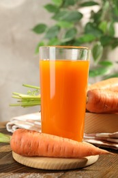 Photo of Healthy carrot juice in glass and fresh vegetables on wooden table