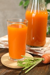 Photo of Healthy carrot juice in glass, bottle and fresh vegetable on wooden table