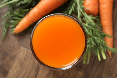 Photo of Healthy carrot juice in glass and fresh vegetables on wooden table, top view