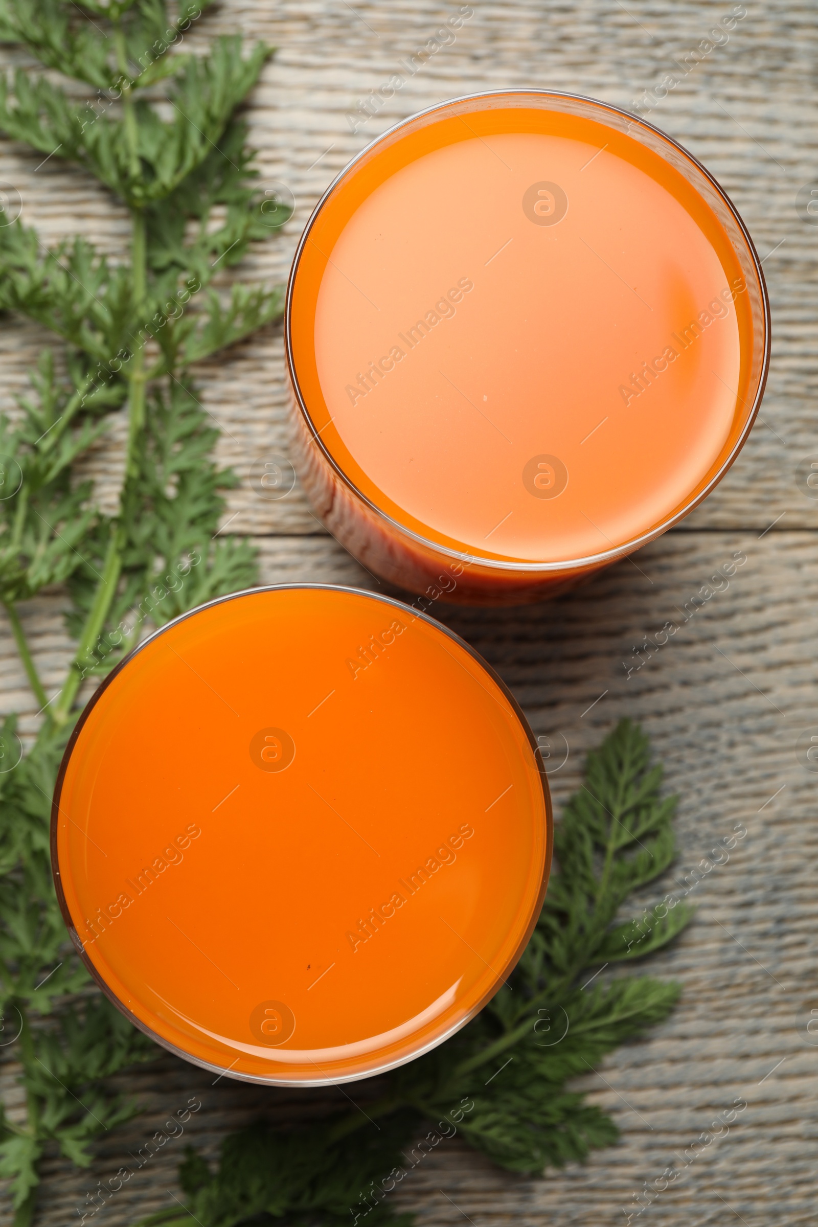 Photo of Healthy carrot juice in glasses and green leaves on wooden table, top view