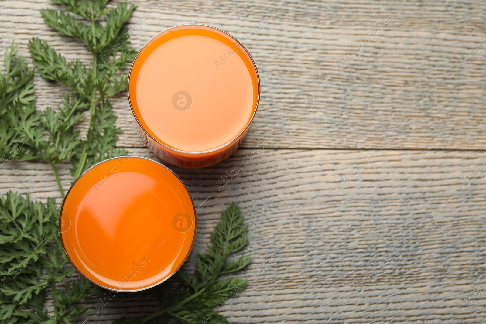 Photo of Healthy carrot juice in glasses and green leaves on wooden table, top view. Space for text