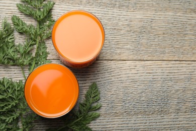 Photo of Healthy carrot juice in glasses and green leaves on wooden table, top view. Space for text