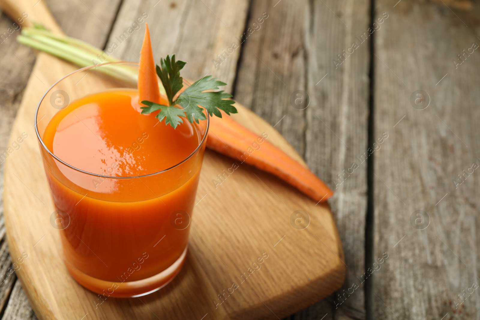 Photo of Healthy juice in glass and fresh carrot on wooden table. Space for text