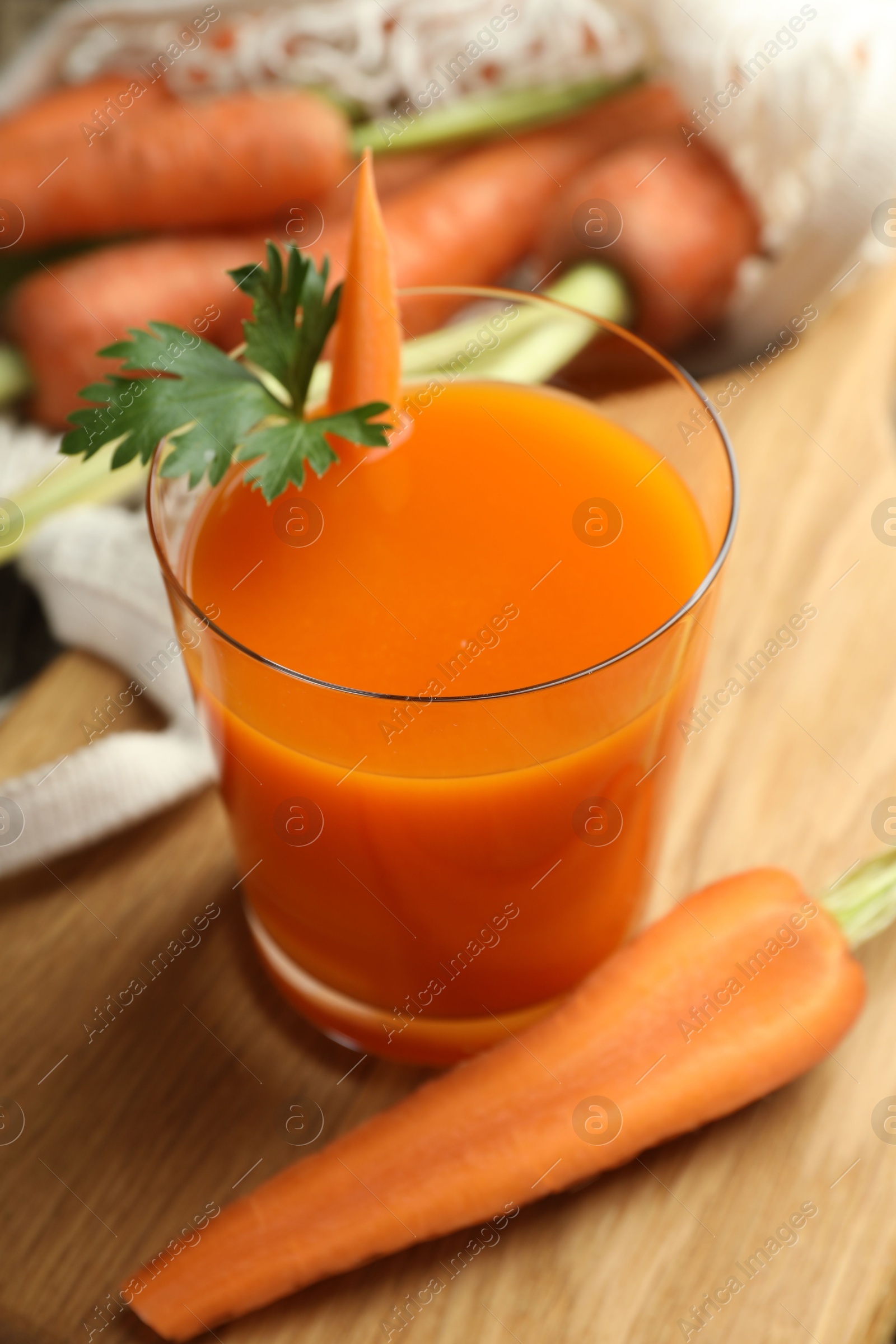 Photo of Healthy juice in glass and fresh carrot on wooden table