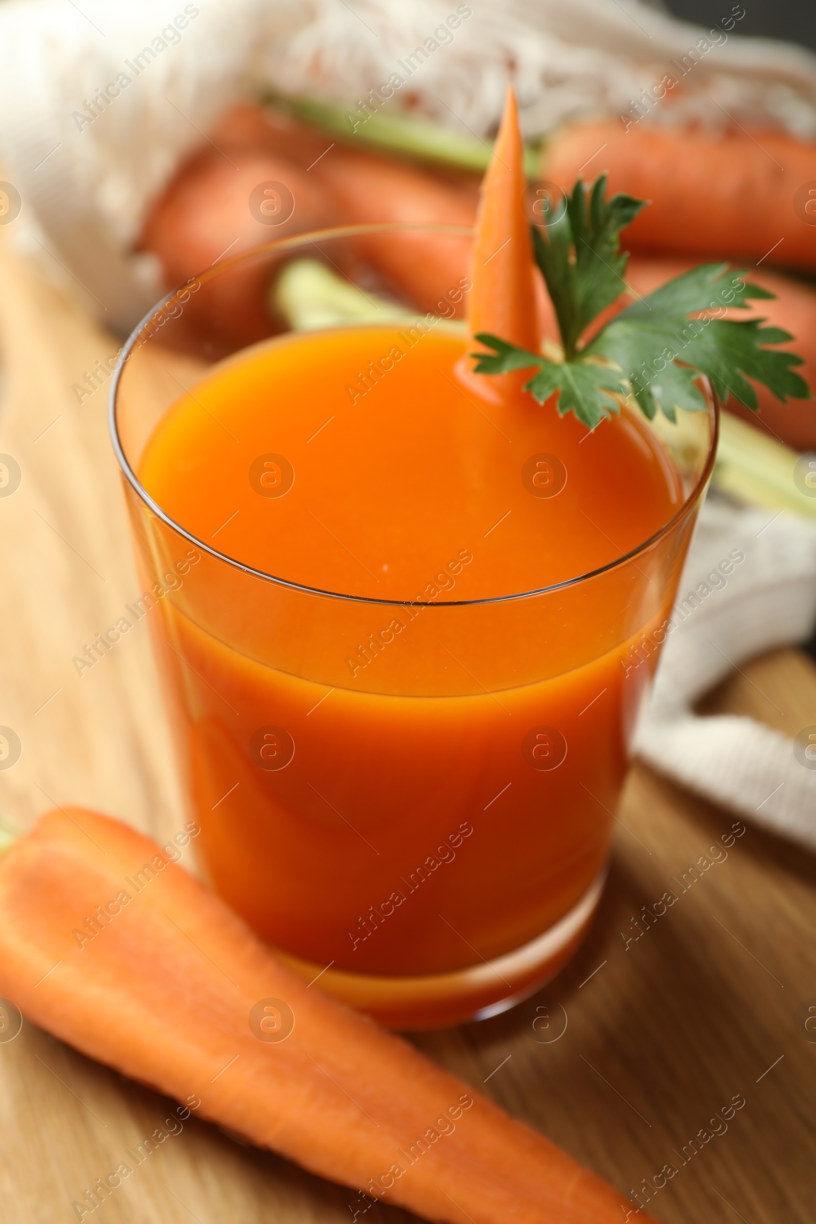 Photo of Healthy juice in glass and fresh carrot on wooden table, closeup