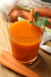 Healthy juice in glass and fresh carrot on wooden table, closeup