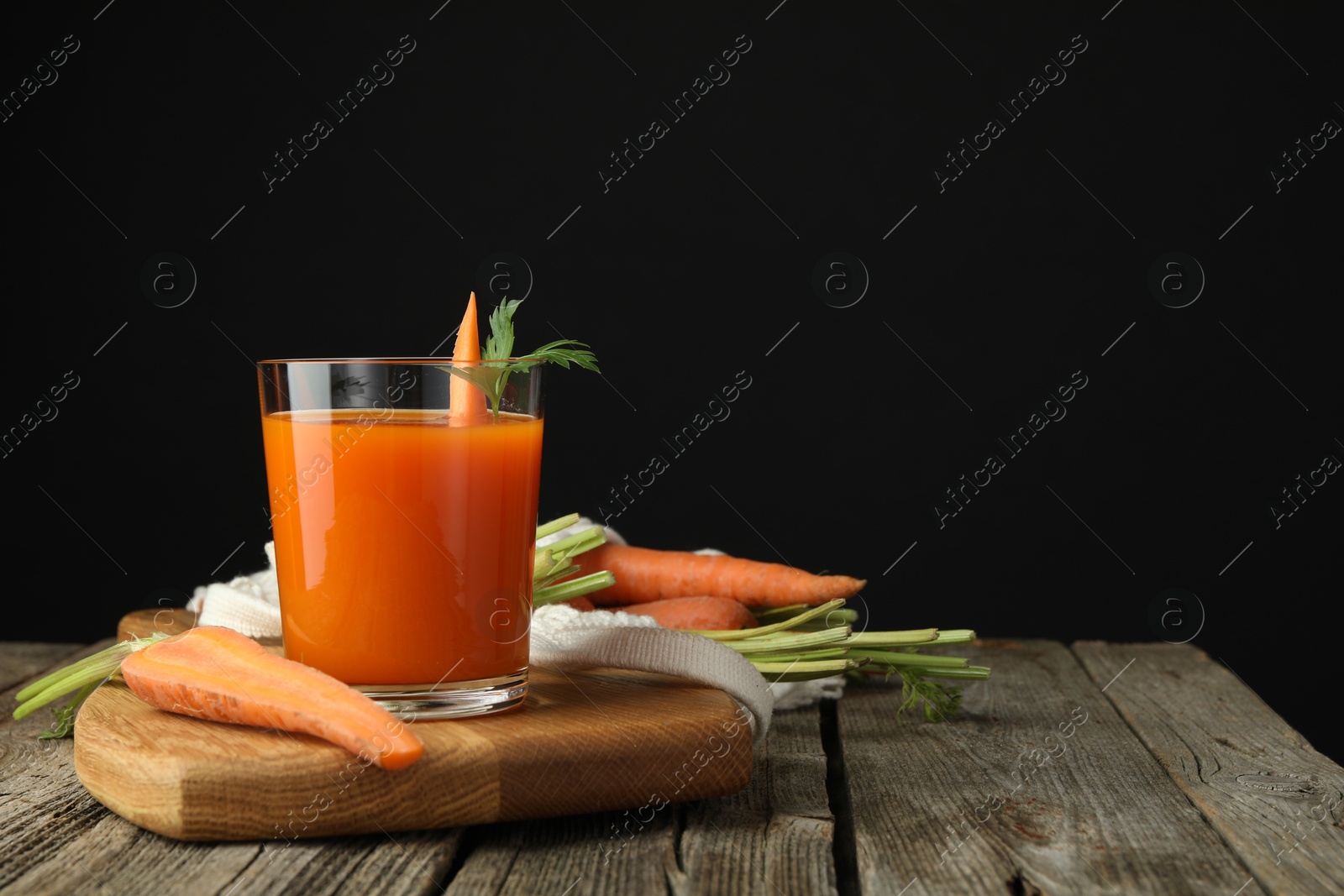 Photo of Healthy juice in glass and fresh carrot on wooden table. Space for text