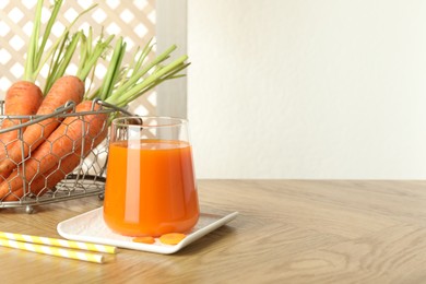 Photo of Healthy juice in glass and fresh carrot on wooden table. Space for text