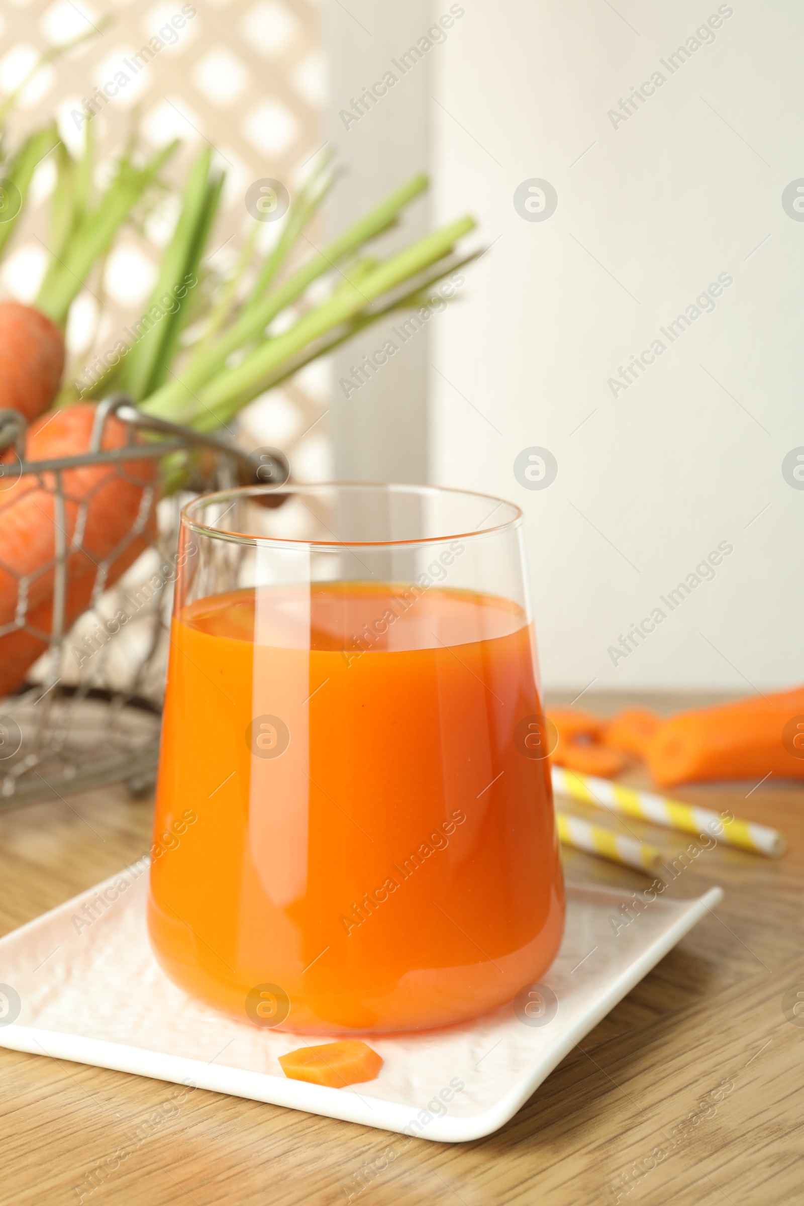 Photo of Healthy juice in glass and fresh carrot on wooden table