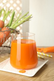 Photo of Healthy juice in glass and fresh carrot on wooden table