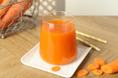 Photo of Healthy juice in glass and fresh carrot on wooden table