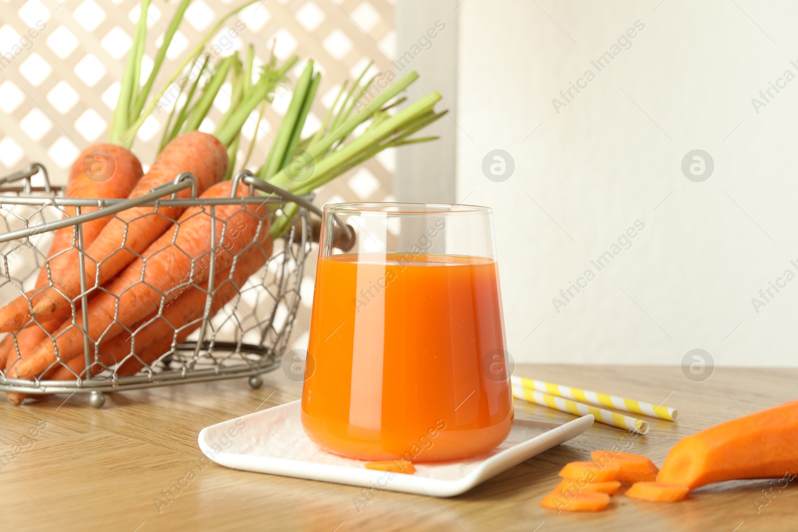 Photo of Healthy juice in glass and fresh carrot on wooden table