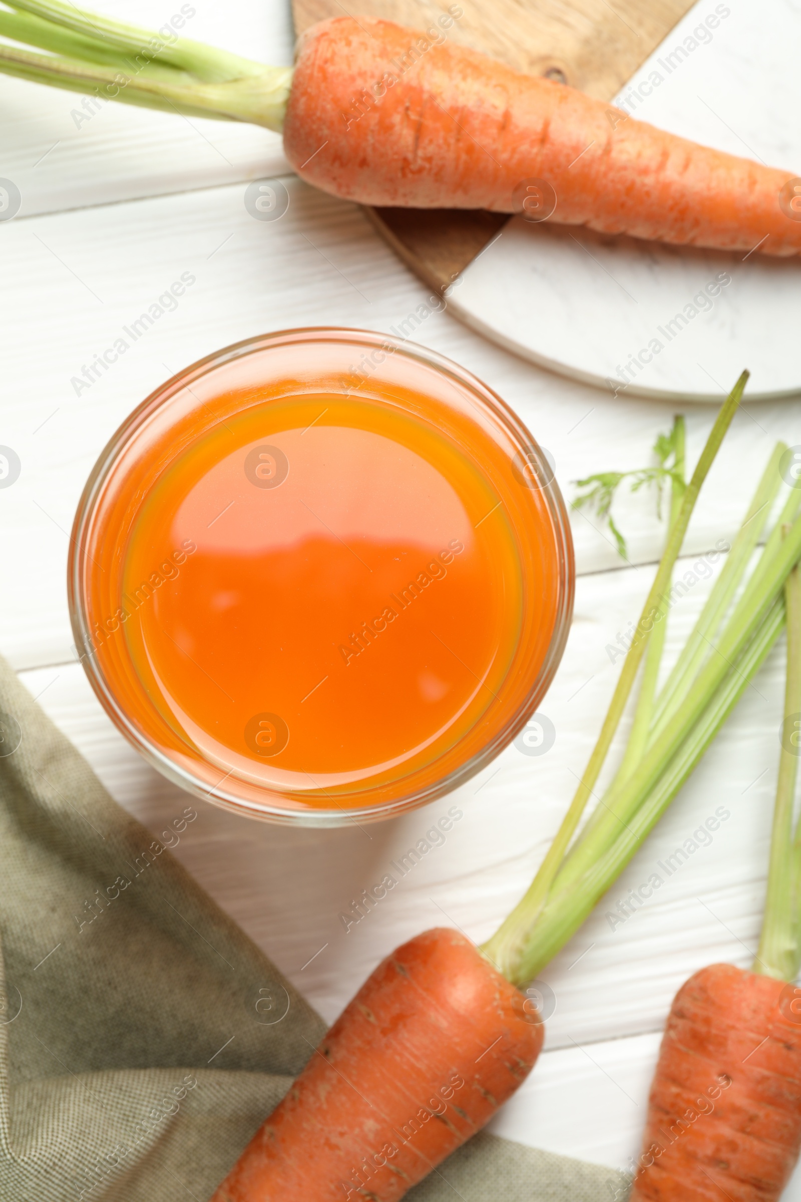 Photo of Healthy juice in glass and fresh carrot on white wooden table, flat lay