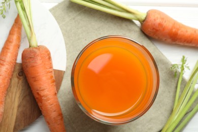 Photo of Healthy juice in glass and fresh carrot on white wooden table, flat lay