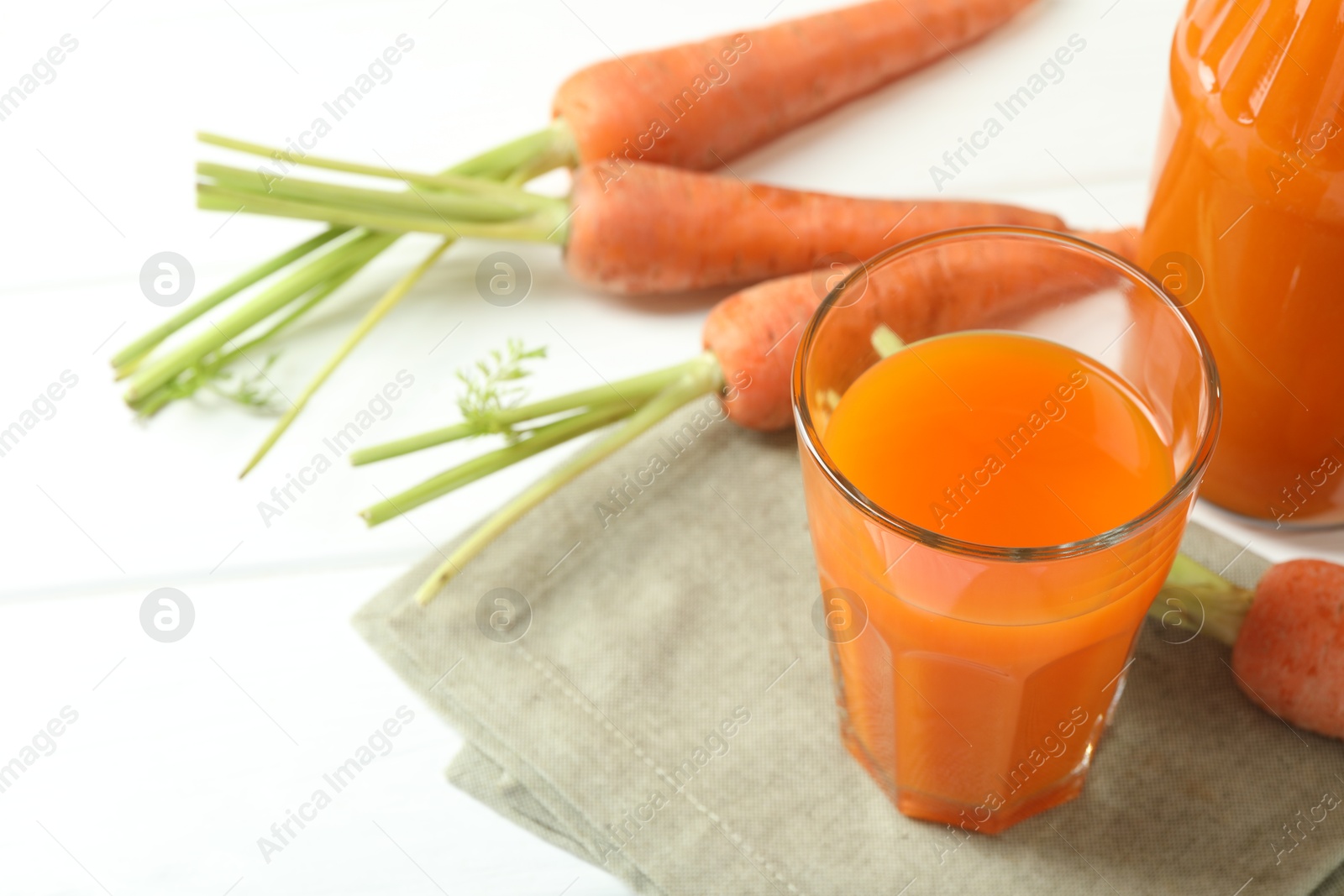 Photo of Healthy juice and fresh carrot on white wooden table. Space for text