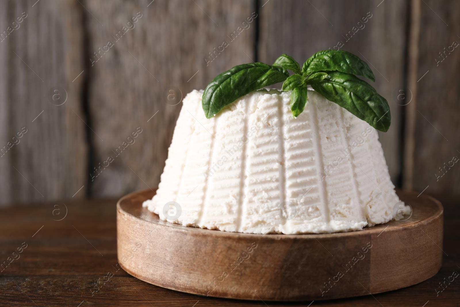 Photo of Fresh ricotta (cream cheese) with basil on wooden table, closeup