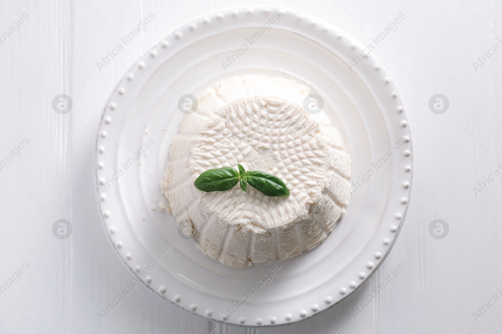 Photo of Fresh ricotta (cream cheese) with basil on white wooden table, top view