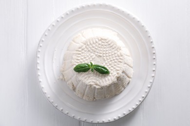 Photo of Fresh ricotta (cream cheese) with basil on white wooden table, top view