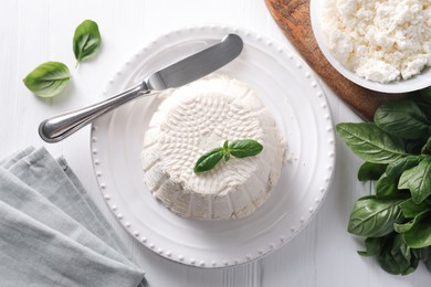 Photo of Fresh ricotta (cream cheese) with basil and knife on white wooden table, flat lay