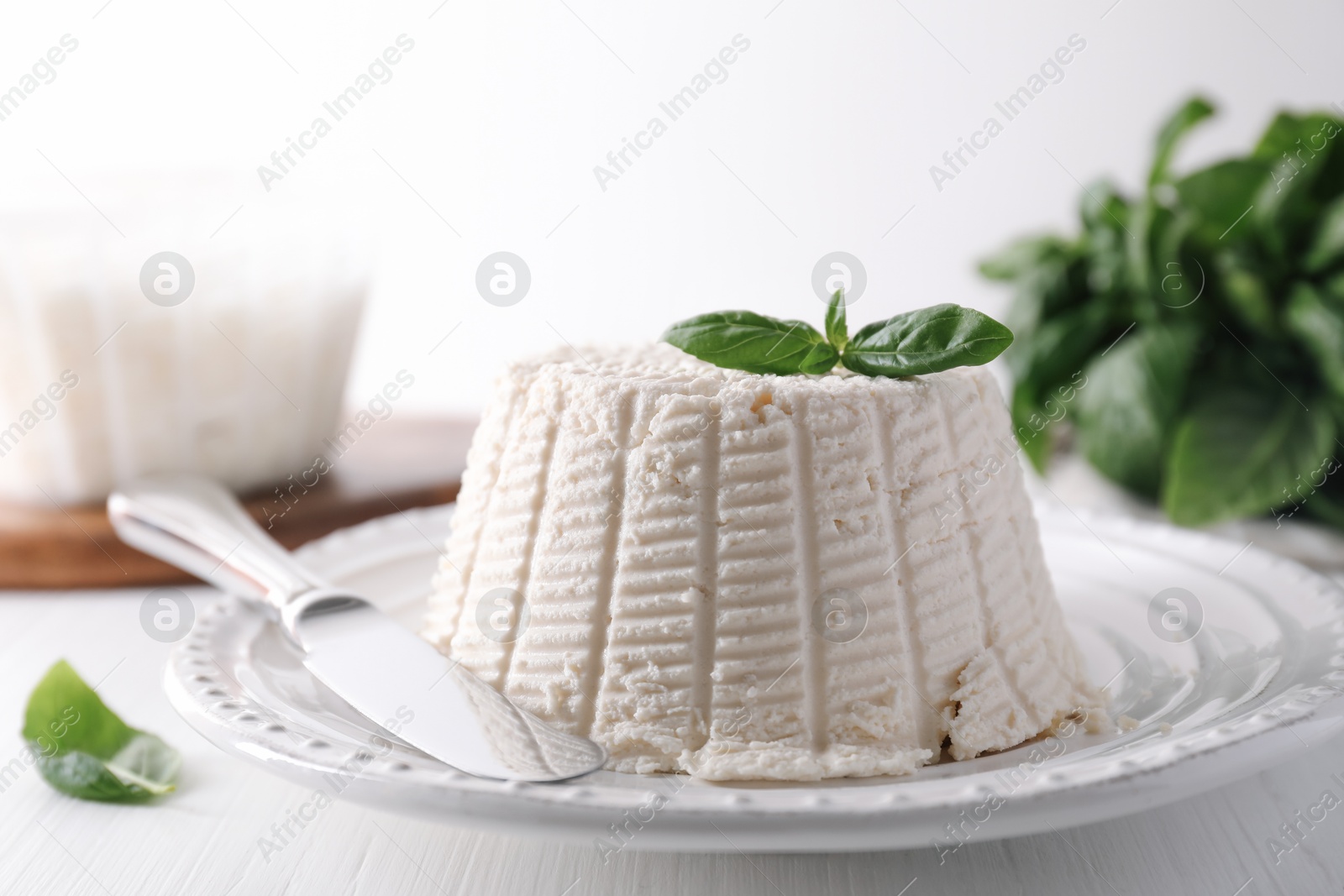 Photo of Fresh ricotta (cream cheese) with basil and knife on white wooden table, closeup