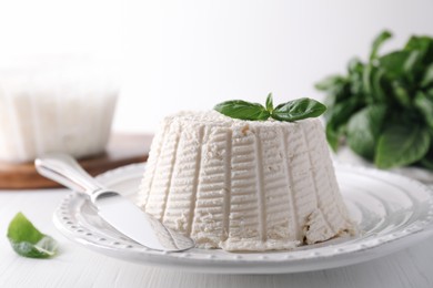 Fresh ricotta (cream cheese) with basil and knife on white wooden table, closeup