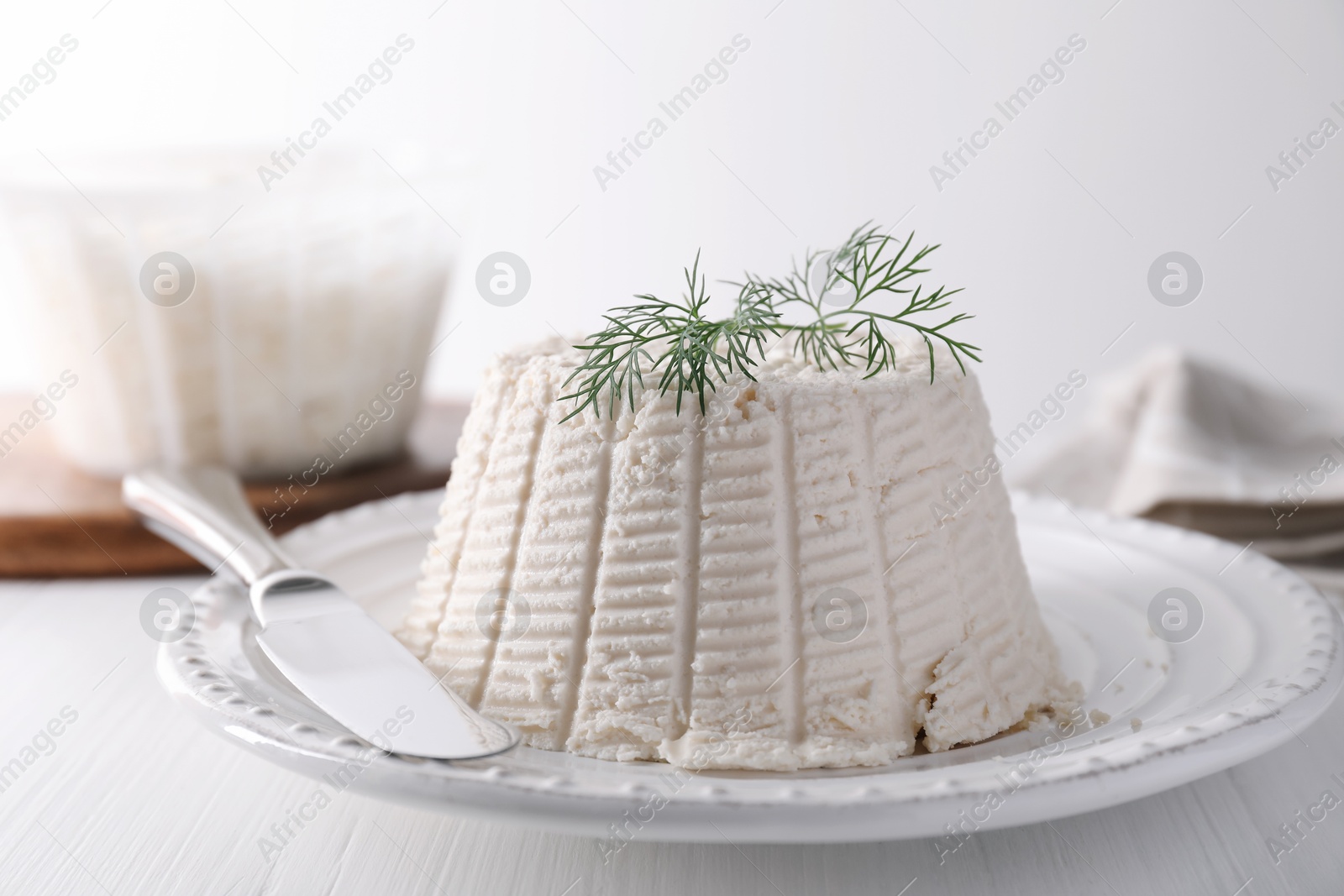 Photo of Fresh ricotta (cream cheese) with dill and knife on white wooden table, closeup