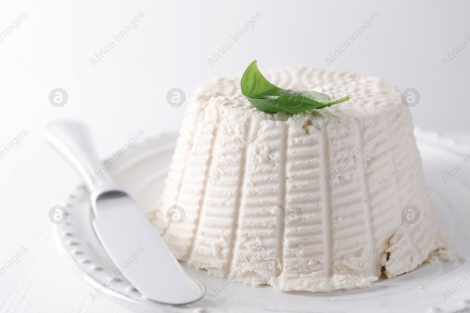 Photo of Fresh ricotta (cream cheese) with basil and knife on white table, closeup