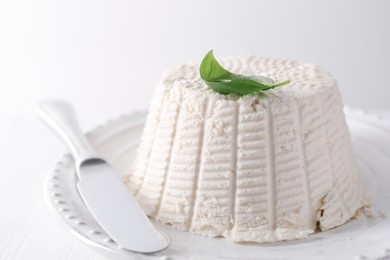 Fresh ricotta (cream cheese) with basil and knife on white table, closeup