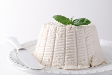 Fresh ricotta (cream cheese) with basil and knife on white table, closeup