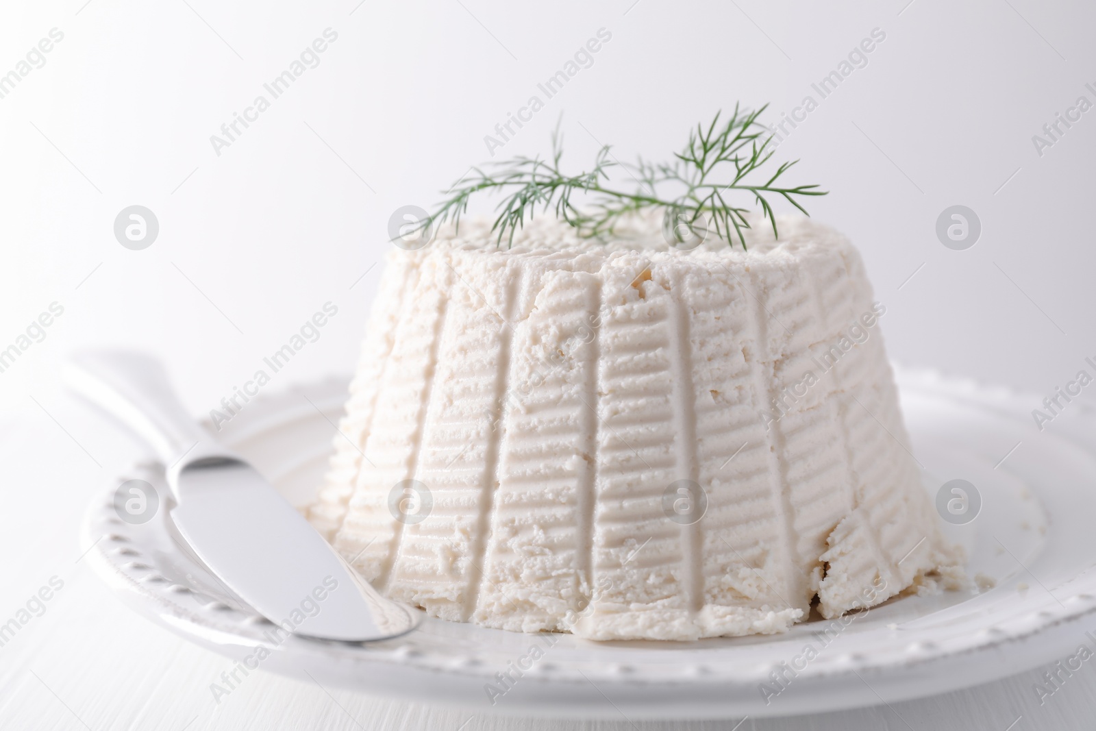 Photo of Fresh ricotta (cream cheese) with dill and knife on white table, closeup