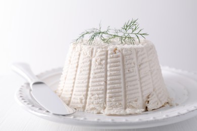 Fresh ricotta (cream cheese) with dill and knife on white table, closeup