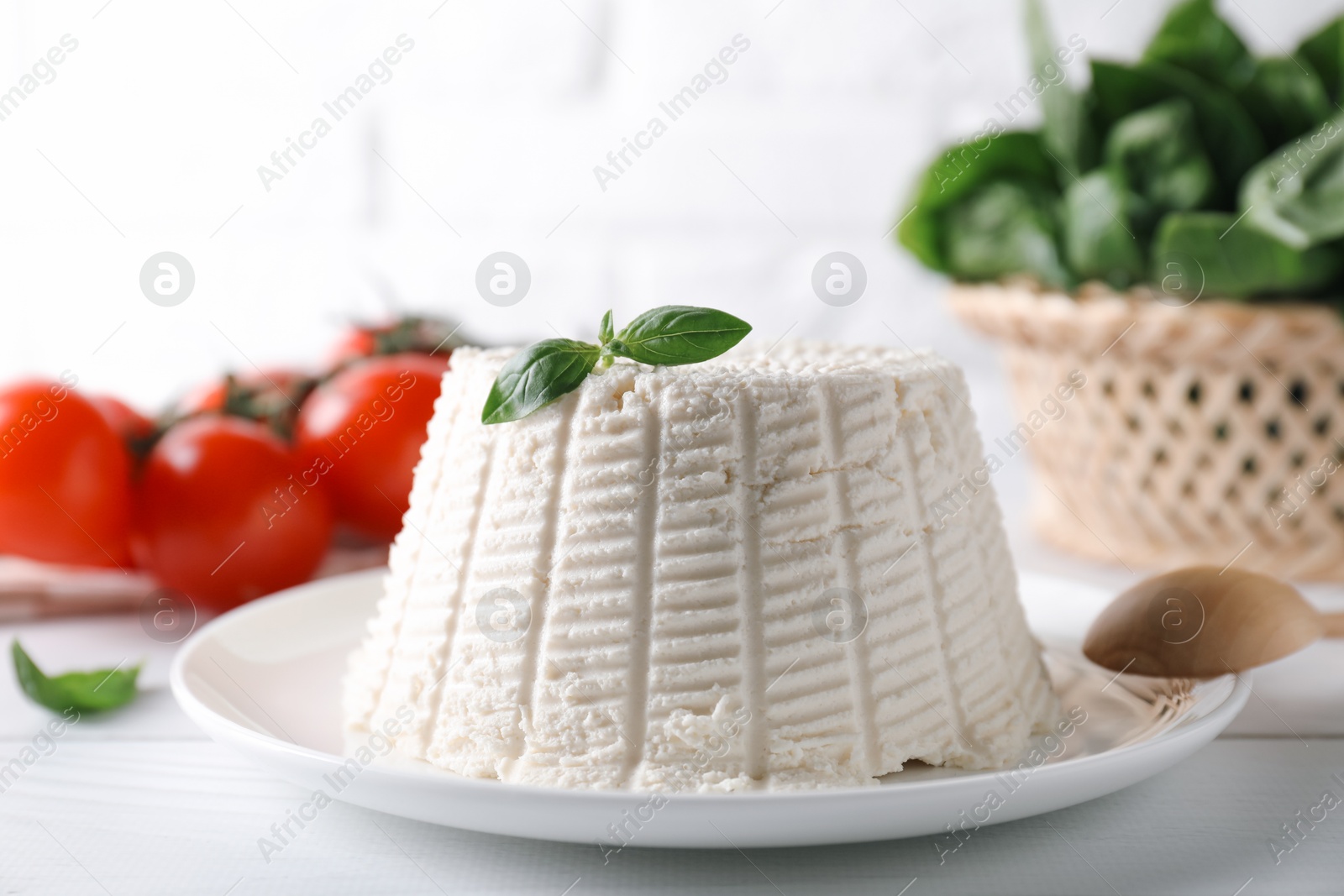 Photo of Fresh ricotta (cream cheese) with basil on white table, closeup