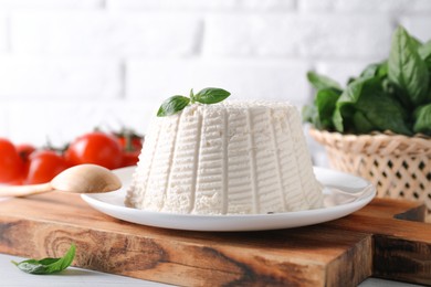 Photo of Fresh ricotta (cream cheese) with basil and spoon on white table